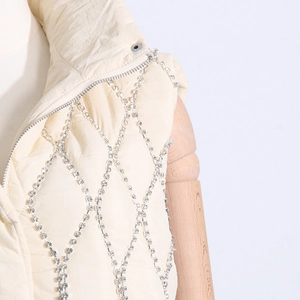 Detail of beige quilted puffer vest featuring sparkling rhinestone chain diamond patterns