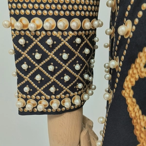 Détails de l'imprimé géométrique doré et des perles blanches brodées sur une manche noire