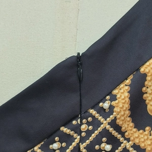 Détail de l'imprimé chaîne dorée et perles avec fermeture éclair invisible sur tissu noir