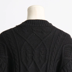 Detail of black cable knit sweater featuring round neckline and thick textured patterns