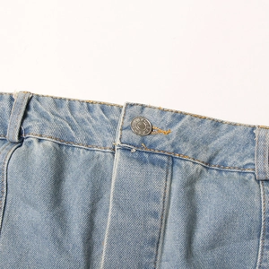 Macro detail of light blue denim waist with silver metal button and belt loops