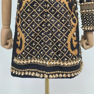 Détails de broderie dorée en losanges et perles blanches sur la robe noire vintage