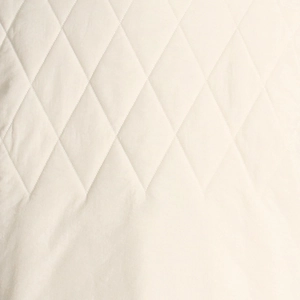 Macro view of ivory quilted vest fabric with classic diamond stitching patterns