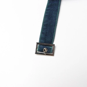 Detailed close-up of dark denim strap with bright green stitching and silver metal buckle