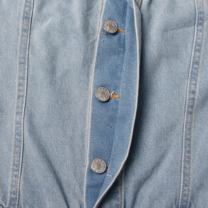 Detail view of light blue denim fabric with silver jeans buttons and orange stitching