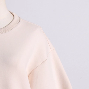 Detailed close-up of ribbed crew neck and drop shoulder seam on beige sweatshirt