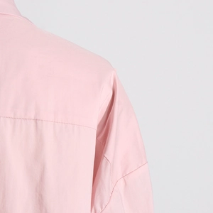 Dettaglio camicia rosa a maniche lunghe con texture del tessuto liscia e cuciture spalla