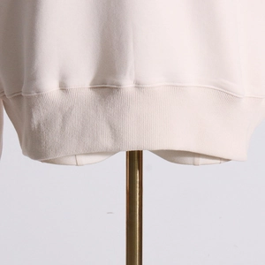 Close-up of cream-colored ribbed hem and stitching on a minimalist design sweatshirt