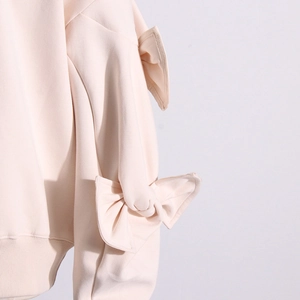 Detail view of the 3D ribbon bow embellishment on a stylish cream pullover sweatshirt