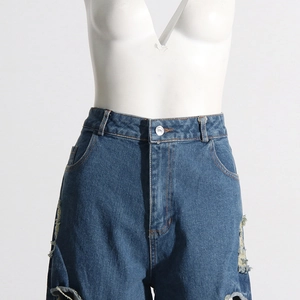 Dettaglio jeans blu a vita alta con strappi laterali e cuciture a contrasto arancioni
