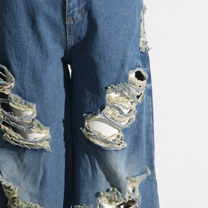 Dettaglio dei graffi pesanti e delle texture strappate sui jeans blu a gamba larga