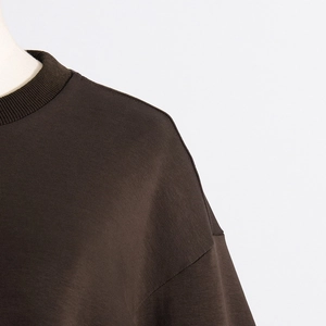 Detail view of the ribbed crewneck and seamless shoulder seams on a dark brown sweatshirt