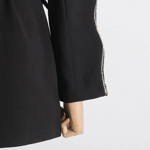 Close-up of black blazer sleeve with rhinestone trim and woven fabric detail