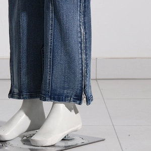 Close-up of washed blue denim hem featuring side metal zipper and vertical topstitching