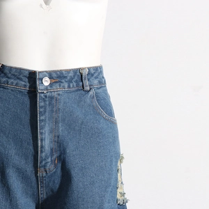 Dettaglio di jeans a vita alta con strappi sfrangiati e bottone in metallo lucido