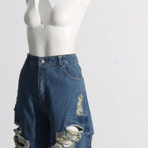 Dettaglio dei jeans blu scuro a vita alta con strappi profondi sulle ginocchia e orli sfrangiati