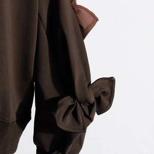 Detail shot of a dark brown sweatshirt featuring a stylish bow on the sleeve and ribbed hem