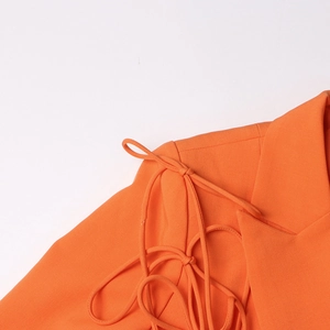 Vue détaillée du blazer orange avec un nœud à cordon élégant sur l'épaule du vêtement