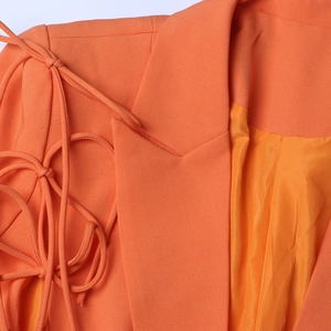 Détail macro d'un blazer orange avec des finitions de laçage aux épaules