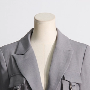 Detail eines grauen Blazers mit flachem Revers, großen Pattentaschen und D-Ring-Akzenten