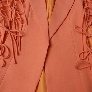 Détail de la manche d'un blazer orange avec découpes et nœuds décoratifs