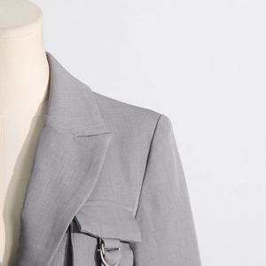 Detail eines grauen Blazers mit steigendem Revers und Tasche mit dekorativem Metallring