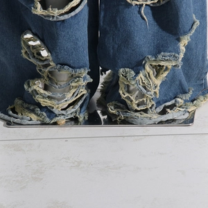Dettaglio del denim blu scuro consumato che mostra i bordi sfrangiati e il design strappato