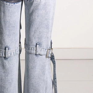 Détail d'un jean délavé bleu clair avec boucle métallique décorative et fermeture éclair