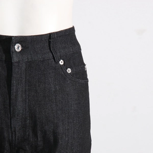 Detail of high waist black denim pants showing the metal button and pocket rivets