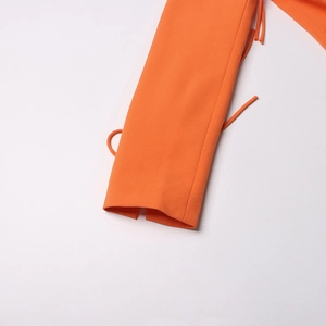 Détail de la manche d'un blazer orange avec nœud décoratif et texture de tissu haut de gamme