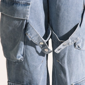 Detail of light blue denim cargo pants showing large side pockets and metal buckle straps