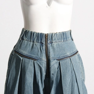 Détail d'un jean bleu clair à taille haute avec design plissé et fermetures éclair