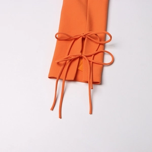 Détail des manches du blazer orange vif avec des nœuds élégants et un tissu de qualité