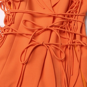 Détail d'un blazer orange vif avec laçage croisé complexe et nœuds décoratifs à la taille