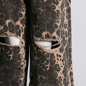 Macro shot of leopard print denim jeans featuring distressed knee holes and frayed edges