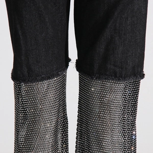 Detailed view of black denim pants featuring heavy rhinestone embellishment and raw edges