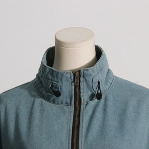 Detail of light blue denim jacket collar with stand-up design and metal drawstring buckle