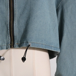 Detail of light blue denim jacket showing metal zipper and adjustable hem drawstring