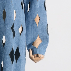 Detail of light blue denim coat featuring diamond cut-outs and frayed cuffs on sleeves
