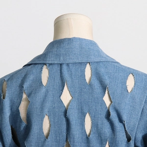 Detail of blue denim coat featuring diamond cutout design and raw frayed edges on the back