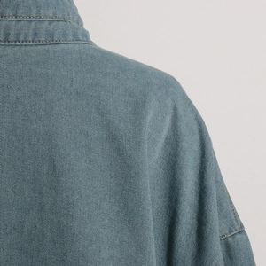 Detailed close-up of collar and shoulder seams on washed blue denim utility jacket