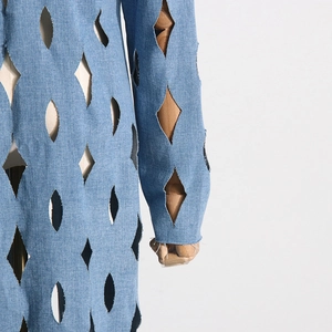 Detail of laser-cut diamond hollow out design and raw hem on light blue denim coat