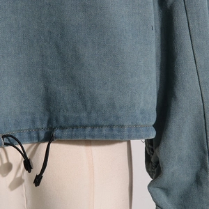 Macro detail of dark blue denim jacket hem featuring adjustable drawstring and stitching