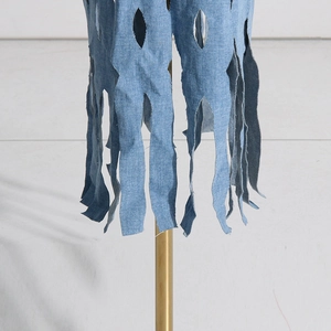 Detail view of light blue denim fabric with diamond cut-outs and fringe texture