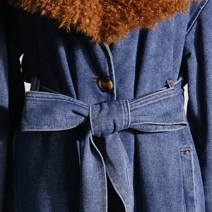 Detailed macro shot of dark blue denim coat featuring brown faux fur collar and amber button