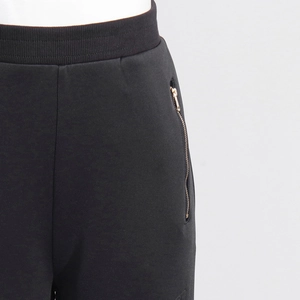 Details einer schwarzen weiten Jogginghose mit geripptem Bund und goldenem Reißverschluss