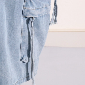 Detail of light blue washed denim skirt showing cargo pocket flap and long decorative strap