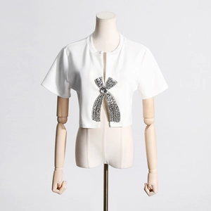 Close-up of a white short-sleeve top featuring a large rhinestone and pearl bow detail