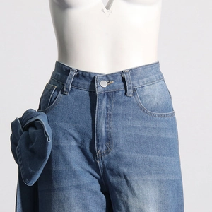 Détail d'un jean bleu à taille haute avec un grand nœud en tissu et un bouton argenté
