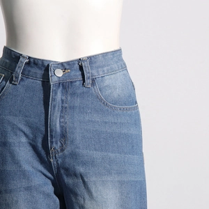 Détail d'un jean bleu taille haute avec bouton argenté et texture de tissu délavé